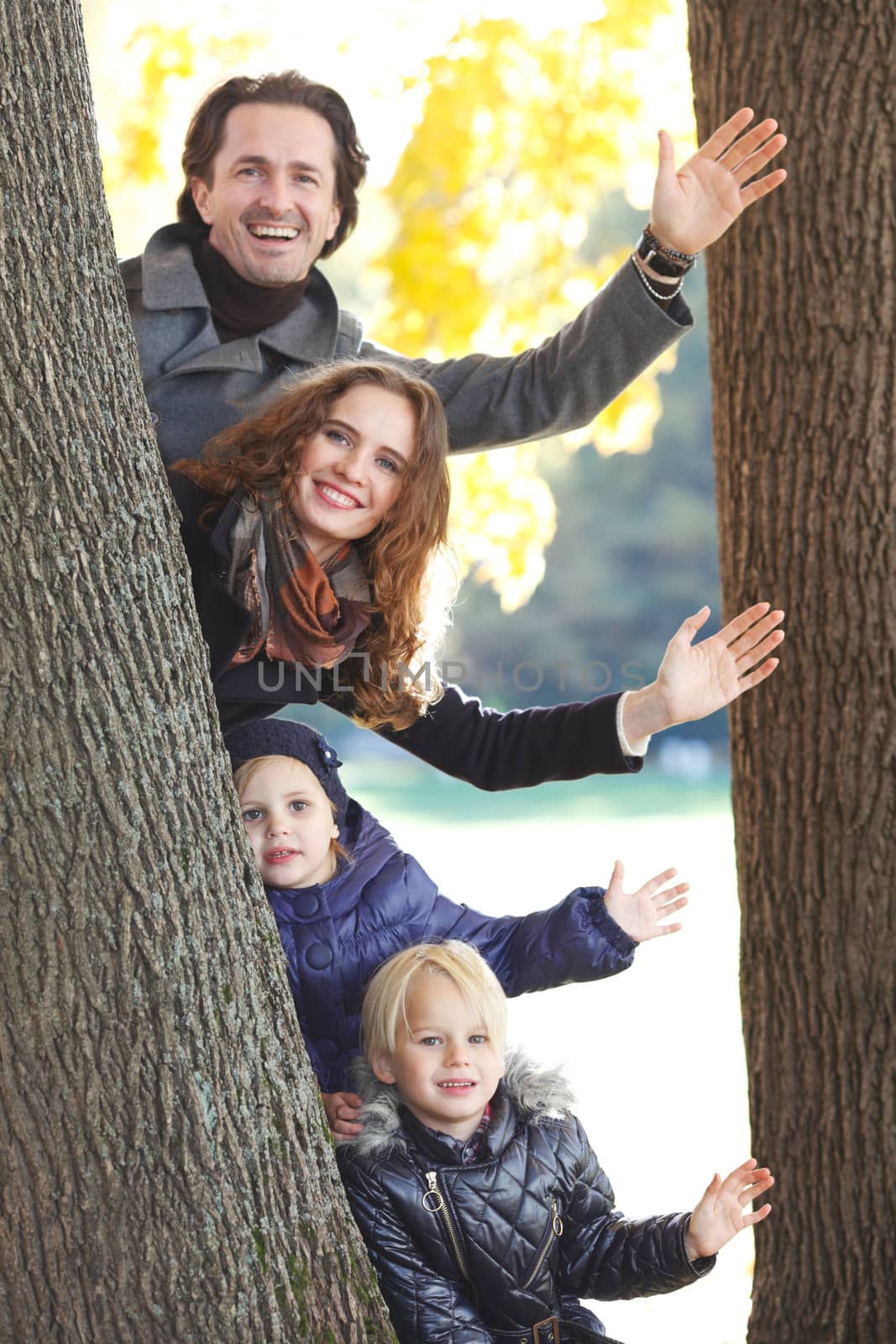 Happy smiling family looking out of tree in autumn park
