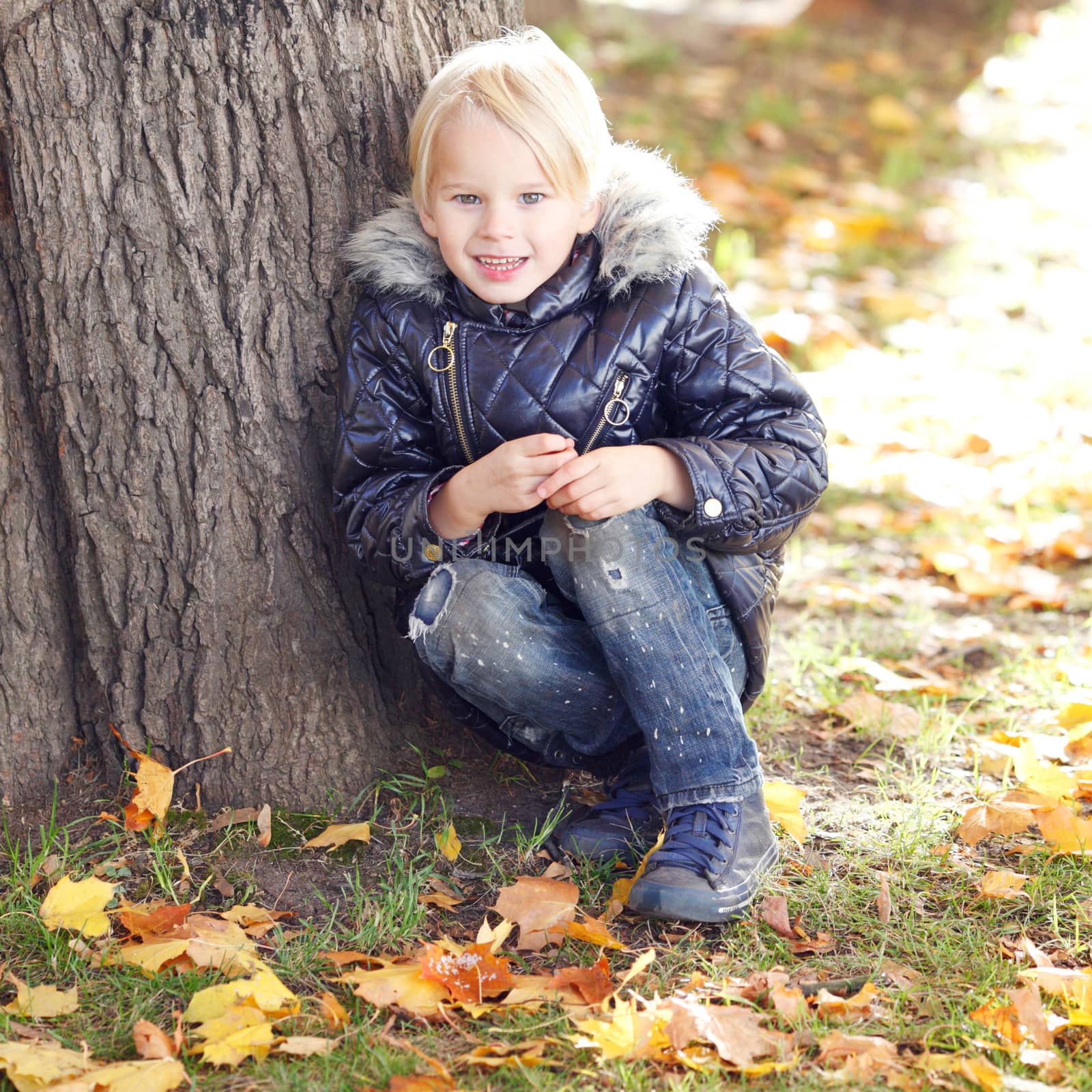 Happy kid sitting near tree in autumn park