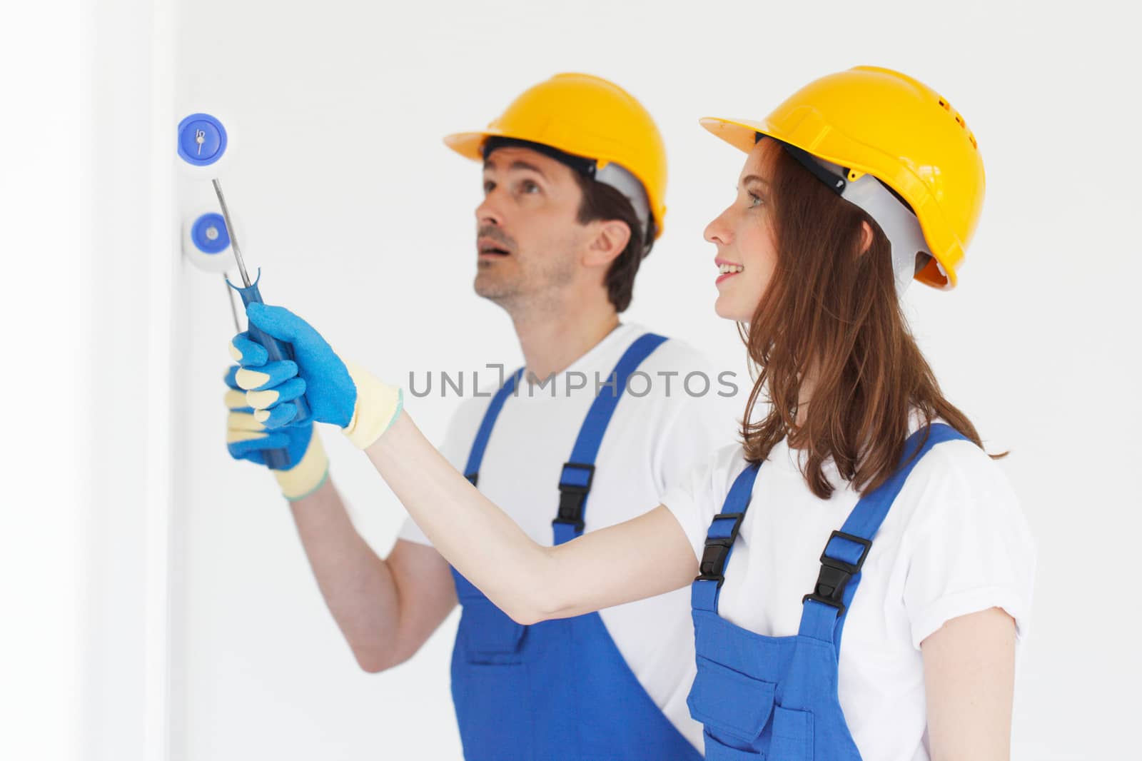 Two workers in helmets painting wall with paint roller