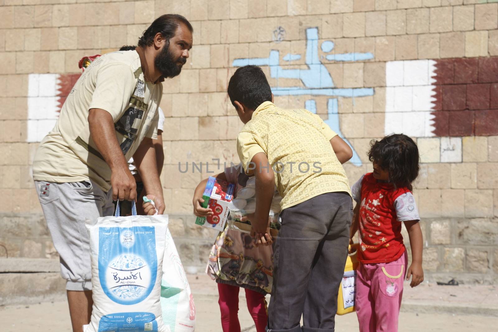 YEMEN, Taiz: A Yemeni man and children carry bags of supplies during a distribution of food and clean water in the Nasser school, outside Taiz (Ta'izz), western Yemen, on October 23, 2015. Many Yemenis are suffering from lack of basic services and resources, in a humanitarian disaster dramatically worsened by a blockade imposed by the Saudi-led coalition.