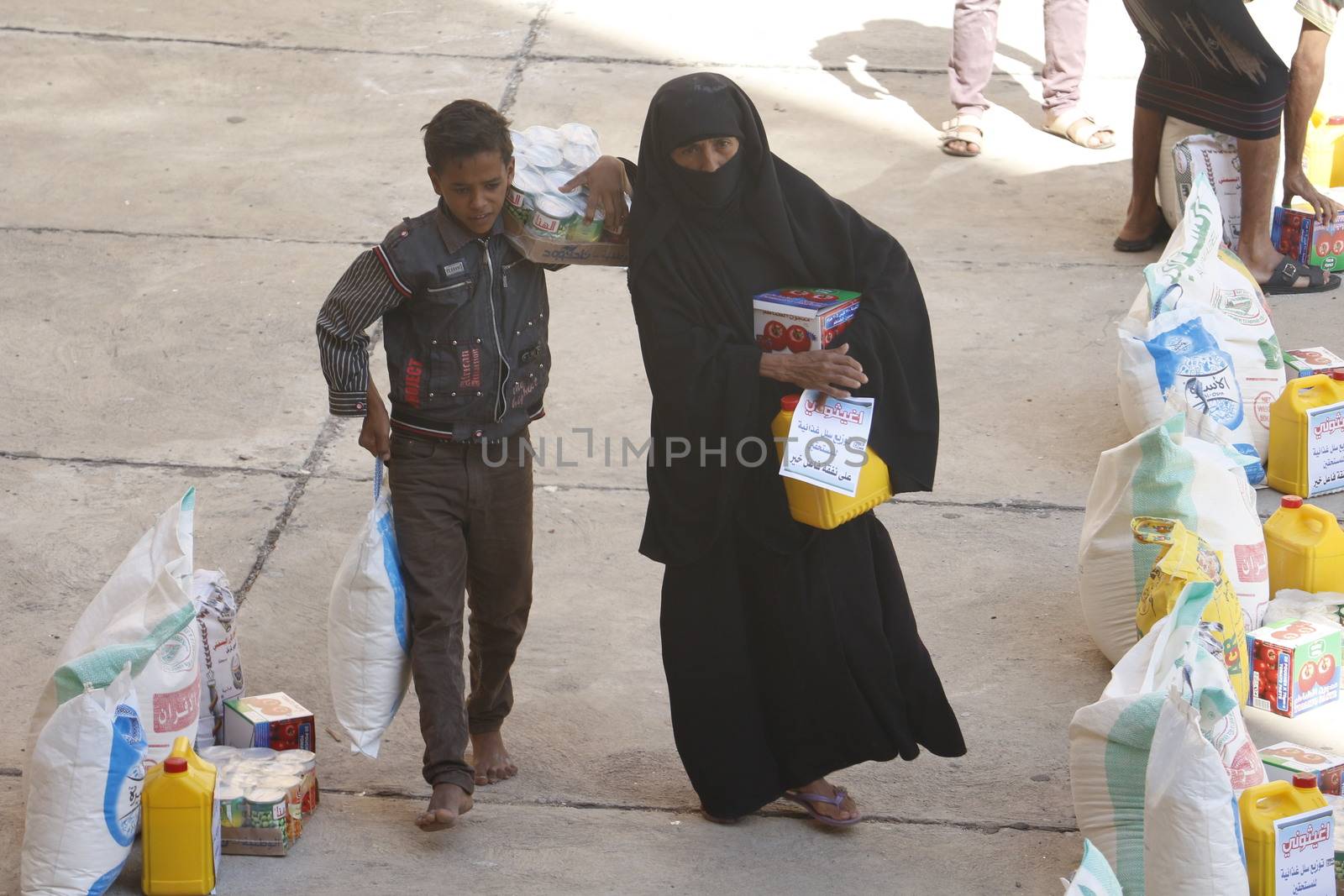 YEMEN, Taiz: A Yemeni woman and her son carry bags of supplies during a distribution of food and clean water in the Nasser school, outside Taiz (Ta'izz), western Yemen, on October 23, 2015. Many Yemenis are suffering from lack of basic services and resources, in a humanitarian disaster dramatically worsened by a blockade imposed by the Saudi-led coalition.