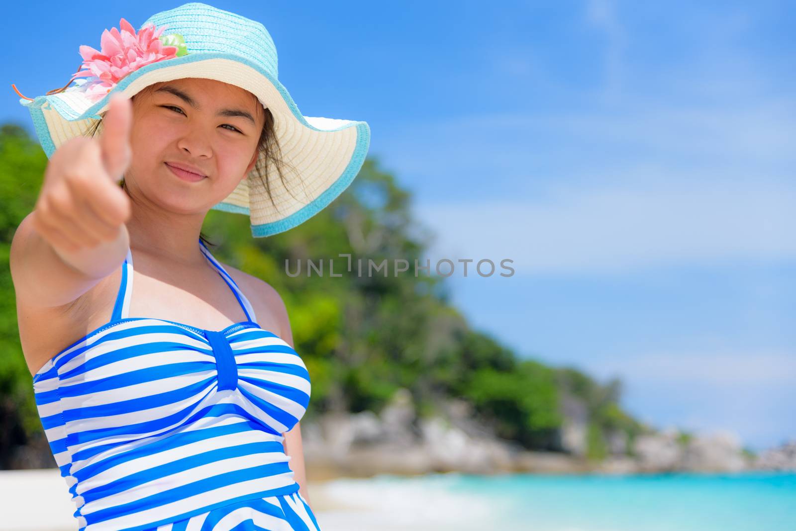Tourist girl in blue white swimsuit standing thumb up praising the natural beauty of the sea on beach during summer at Koh Miang Island, Mu Ko Similan National Park, Phang Nga Province, Thailand