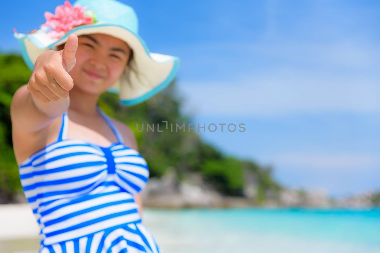 Tourist girl in blue white swimsuit standing thumb up praising the natural beauty of the sea on beach during summer at Koh Miang Island, Mu Ko Similan National Park, Phang Nga Province, Thailand