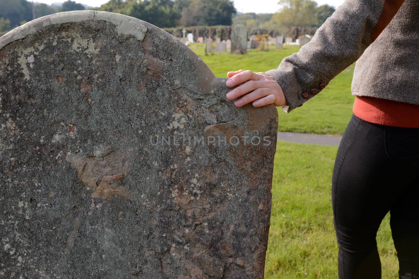 Woman's hand resting on an anonymous headstone in a rural graveyard