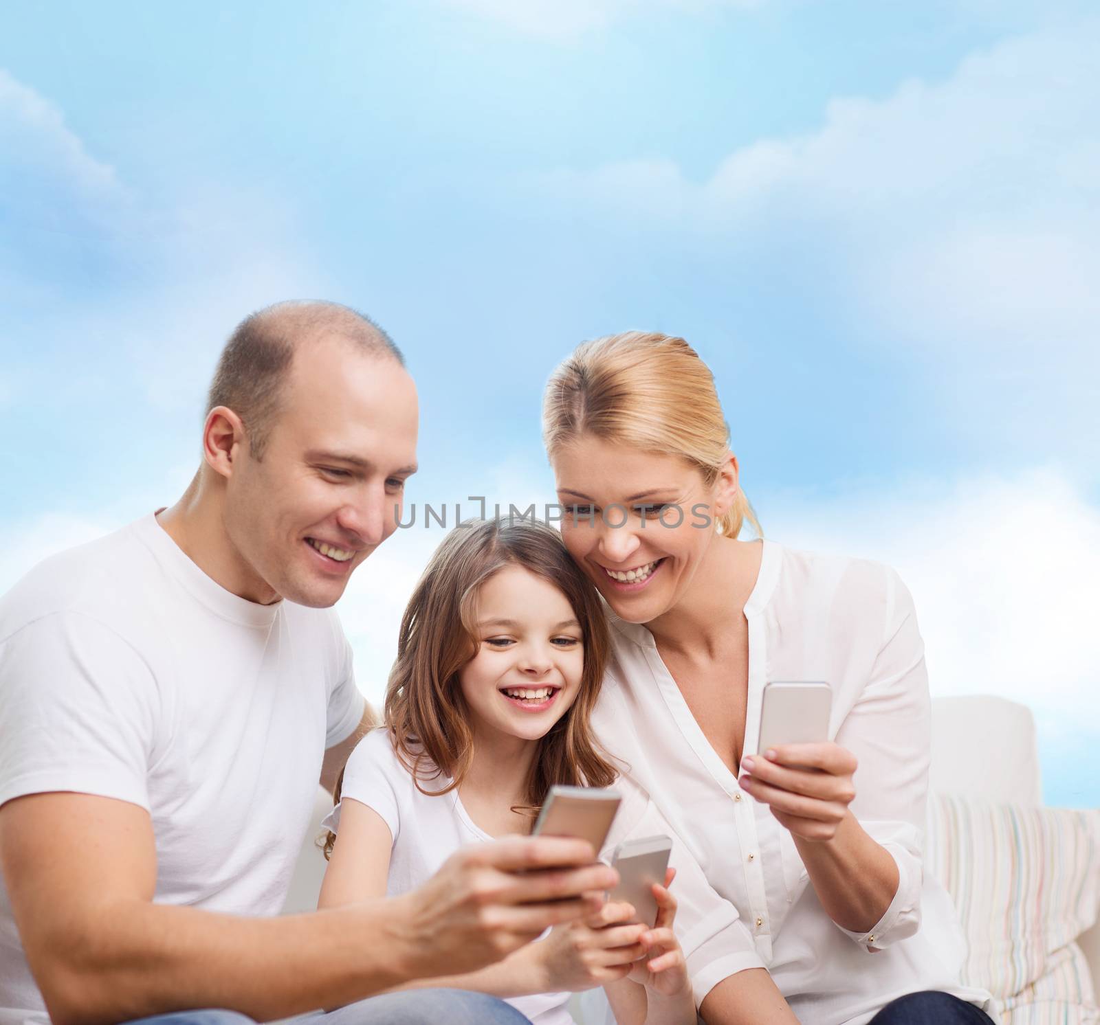 family, technology and people concept - smiling mother, father and little girl with smartphones over blue sky background