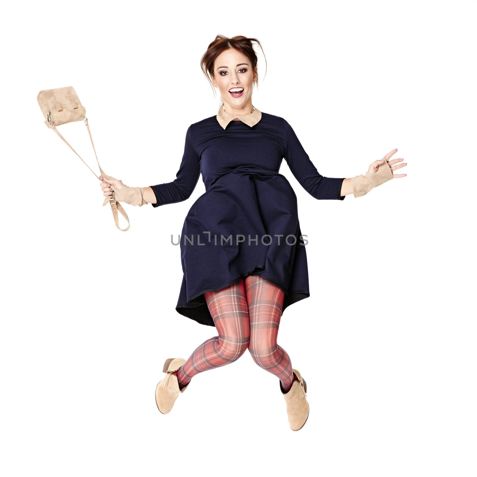 Young woman in dark blue dress and checkered tights is jumping over white background.