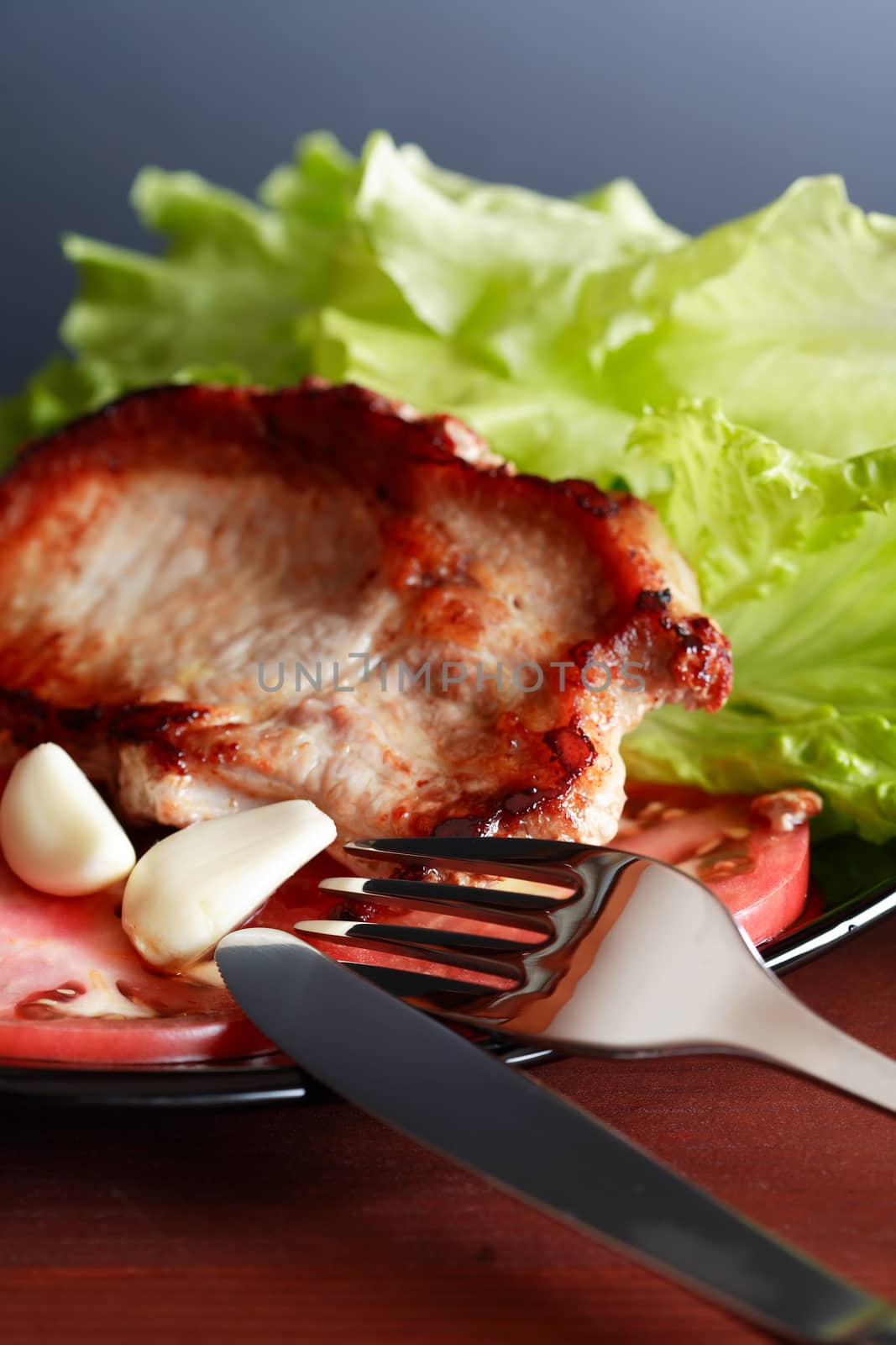 Piece of roasted meat on plate near tomato and green salad