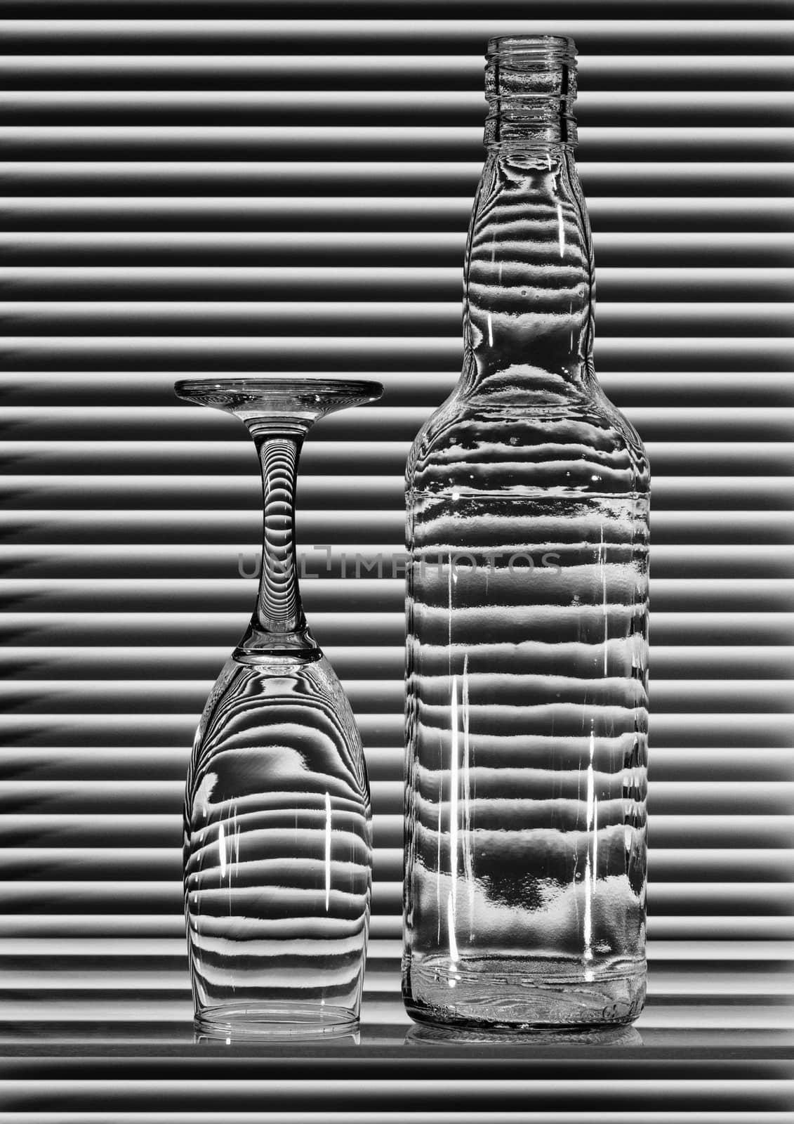 Empty bottle and turned glass with bands of reflection blinds