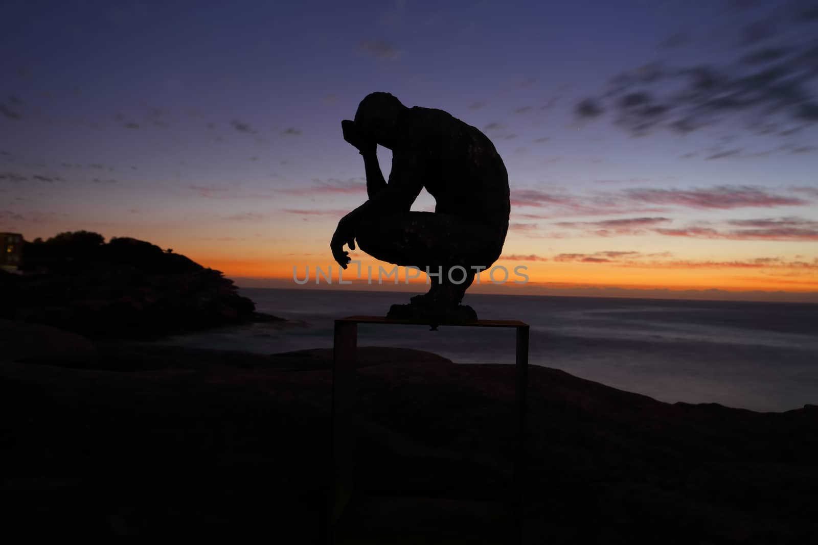 BONDI, AUSTRALIA - OCTOBER 25, 2015;  Annual Sculpture by the Sea free public event.  Exhibit titled Crouching Man by Laurence Edwards.    Made of bronze. Silhouette against dawn sky