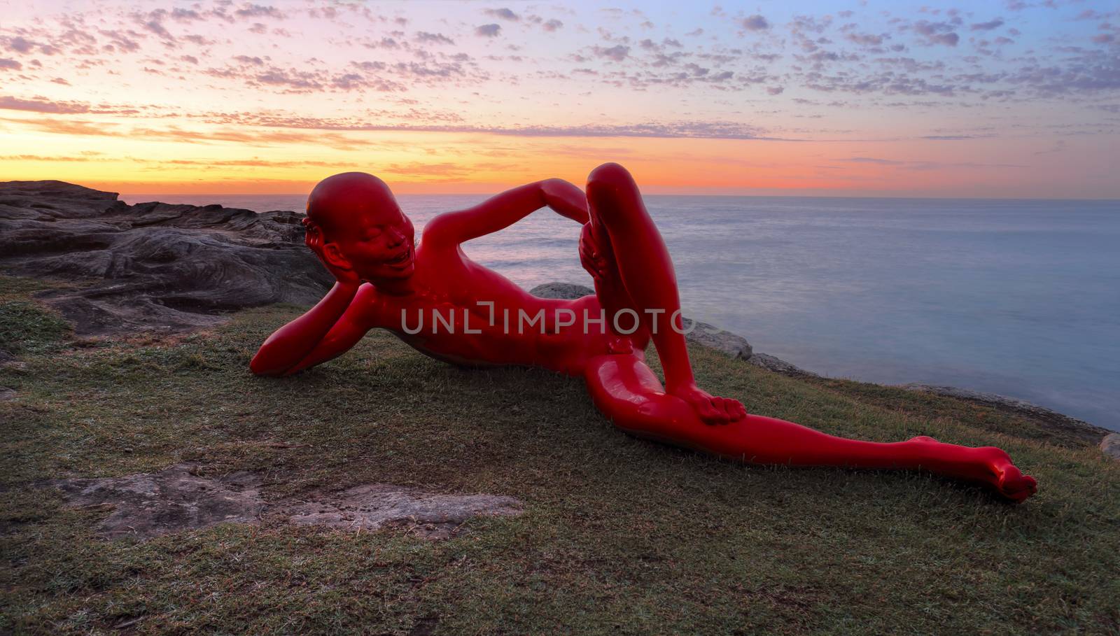 BONDI, AUSTRALIA - OCTOBER 25, 2015;  Annual Sculpture by the Sea  public event.  Exhibit titled Harbour by Chen Wenline, a glossy painted bronze figure with cheeky expression and pose against a sunrise sky