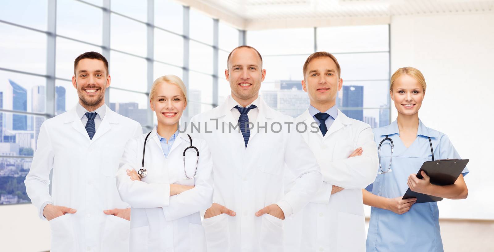 medicine, profession, teamwork and healthcare concept - group of smiling medics or doctors with clipboard and stethoscopes over clinic background