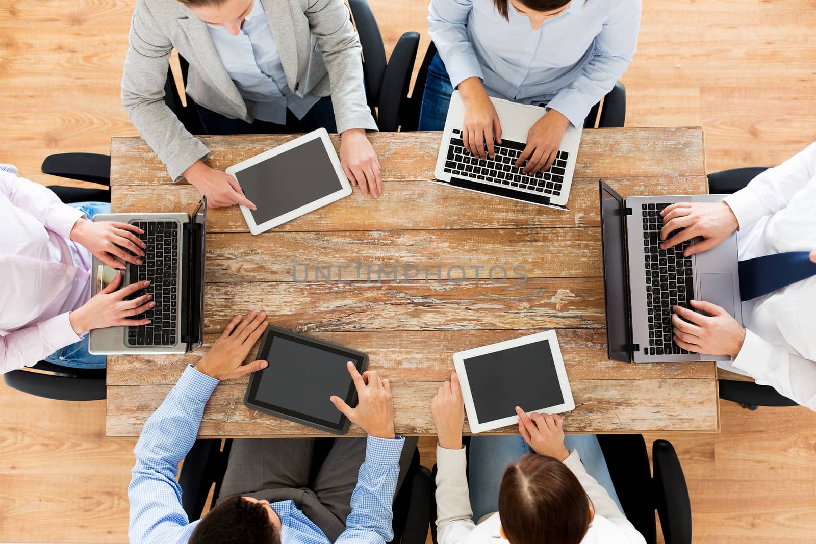 business, people and technology concept - close up of creative team with laptop and tablet pc sitting at table in office