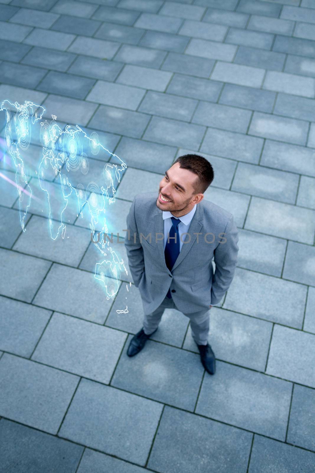 business, development and people concept - young smiling businessman with world map hologram outdoors from top