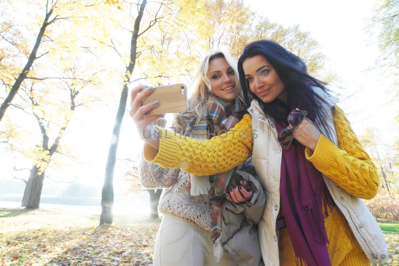 Beautiful young women taking a selfie with smartphone outdoors in park in autumn