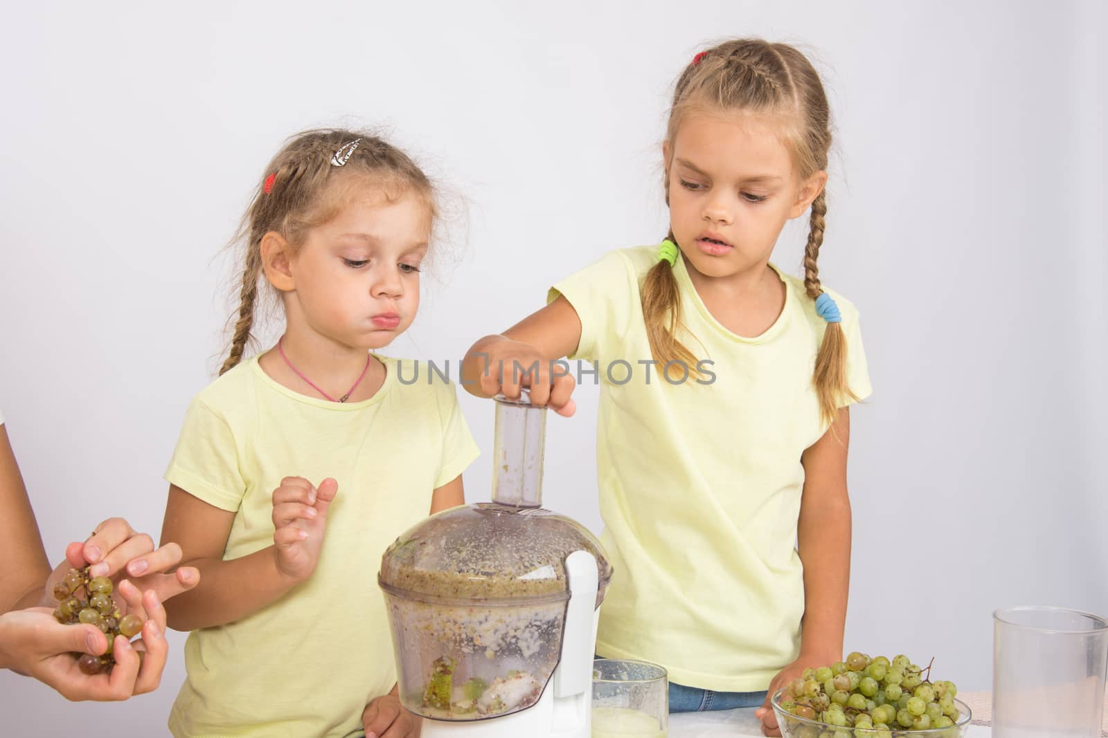 Two girls at a table squeezed juice from pears and grapes with a juicer