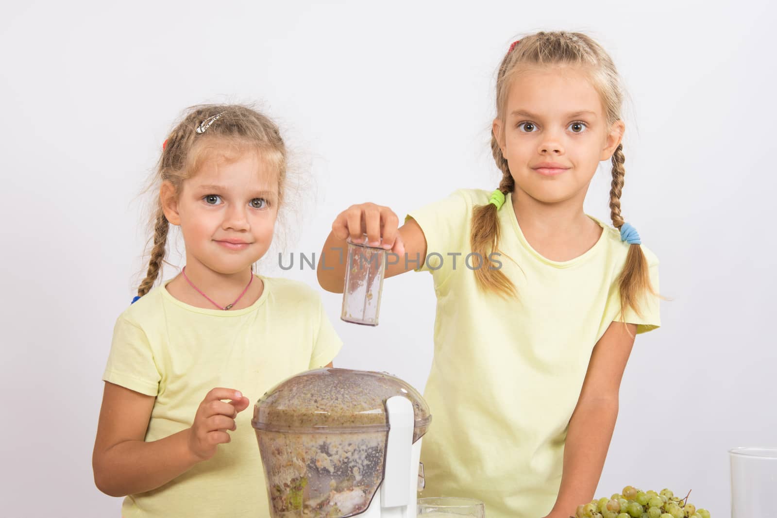 Two girls at a table squeezed juice from pears and grapes with a juicer