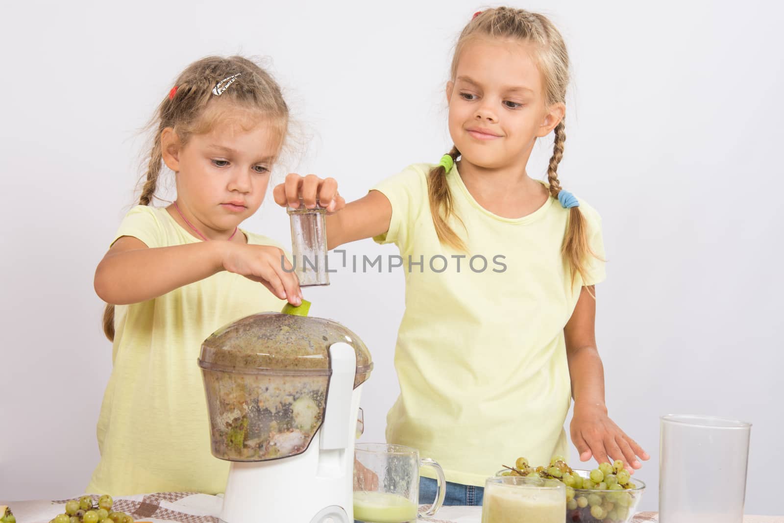 Two girls at a table squeezed juice from pears and grapes with a juicer