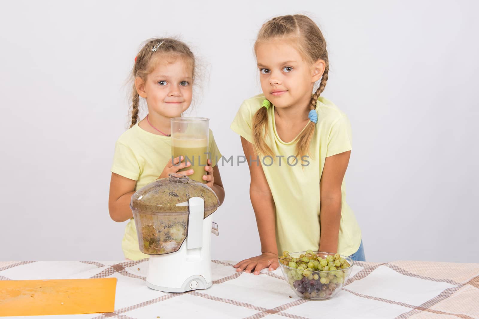 Two girls at a table squeezed juice from pears and grapes with a juicer