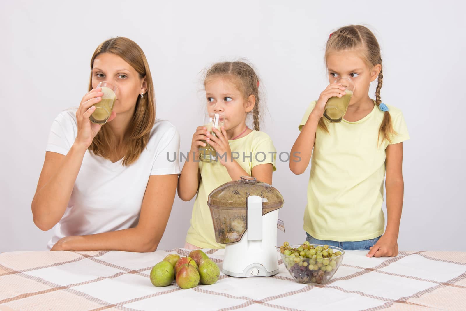 Young beautiful mother and two daughters sitting at a table squeezed juice from pears and grapes with a juicer