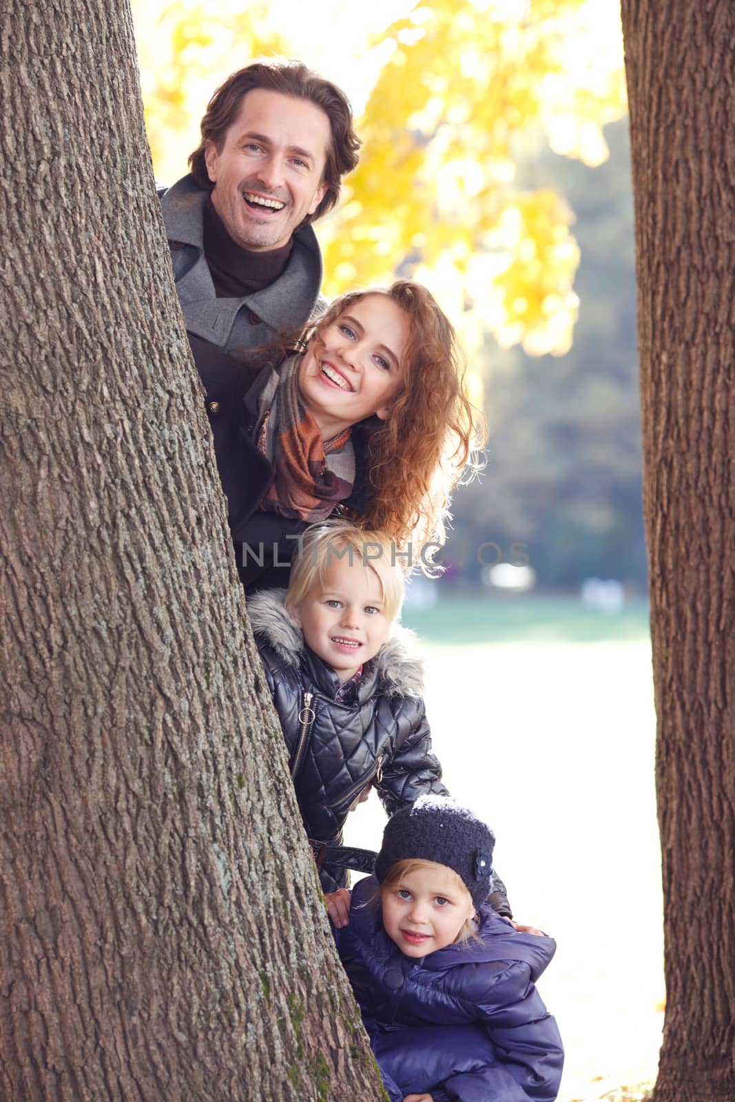 Happy smiling family looking out of tree in autumn park