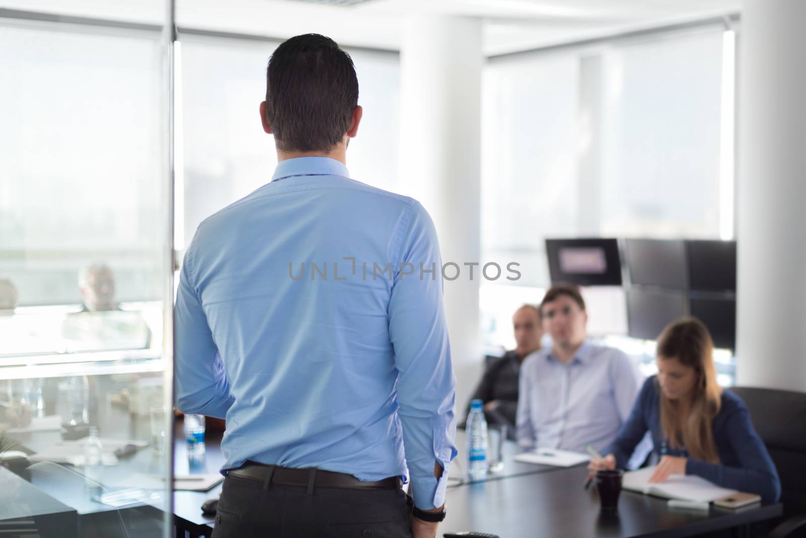 Business man making a presentation at office. Business executive delivering a presentation to his colleagues during meeting or in-house business training. Rear view. Shalow depth of field.