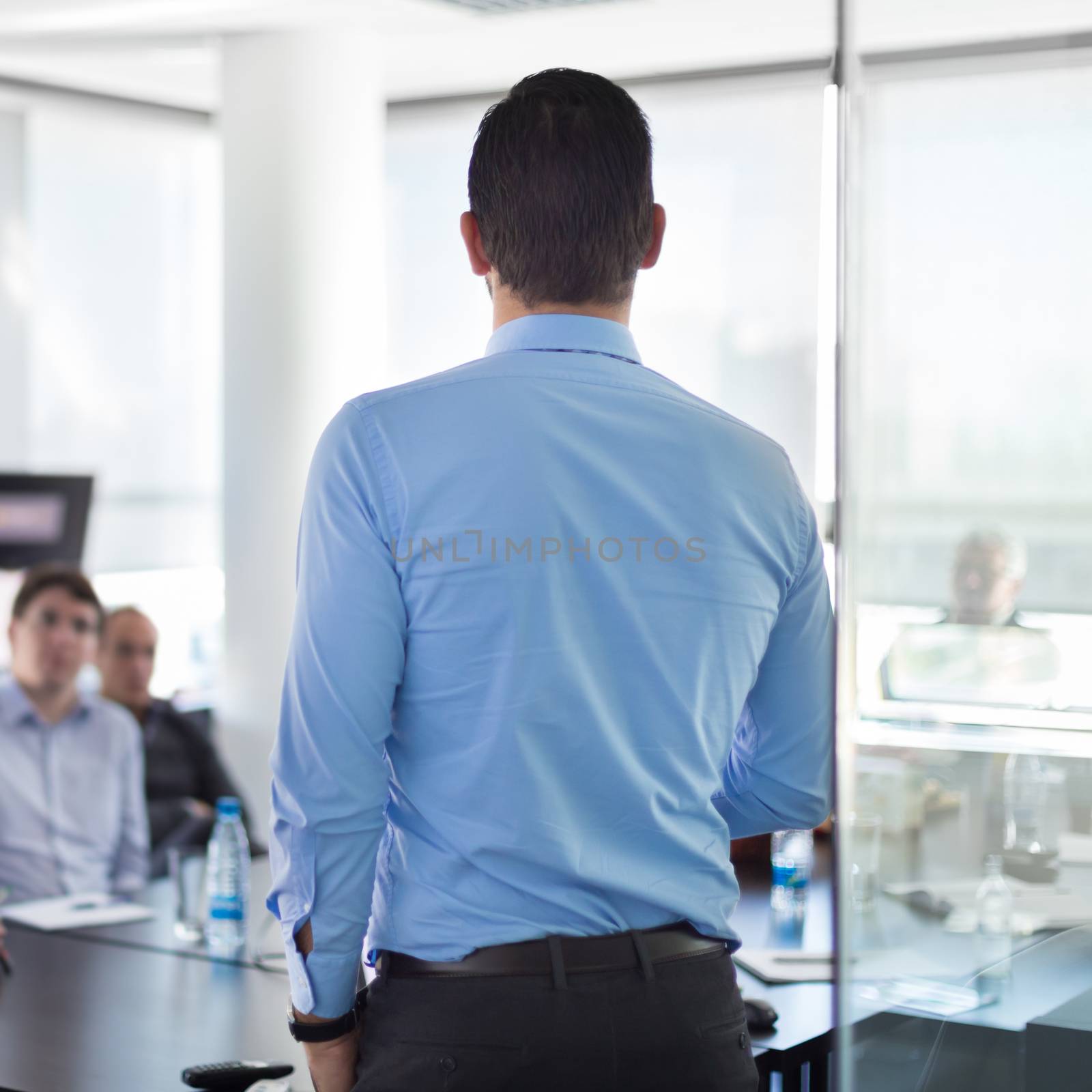 Business man making a presentation at office. Business executive delivering a presentation to his colleagues during meeting or in-house business training. Rear view. Shalow depth of field.