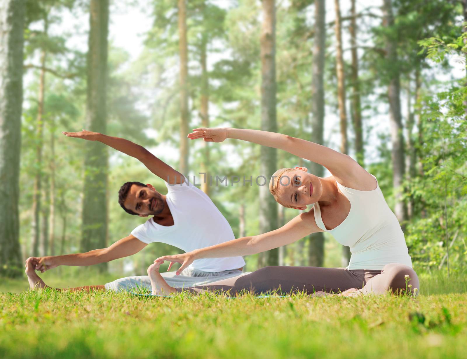 fitness, sport, yoga and people concept - happy couple stretching on mats over green woods background
