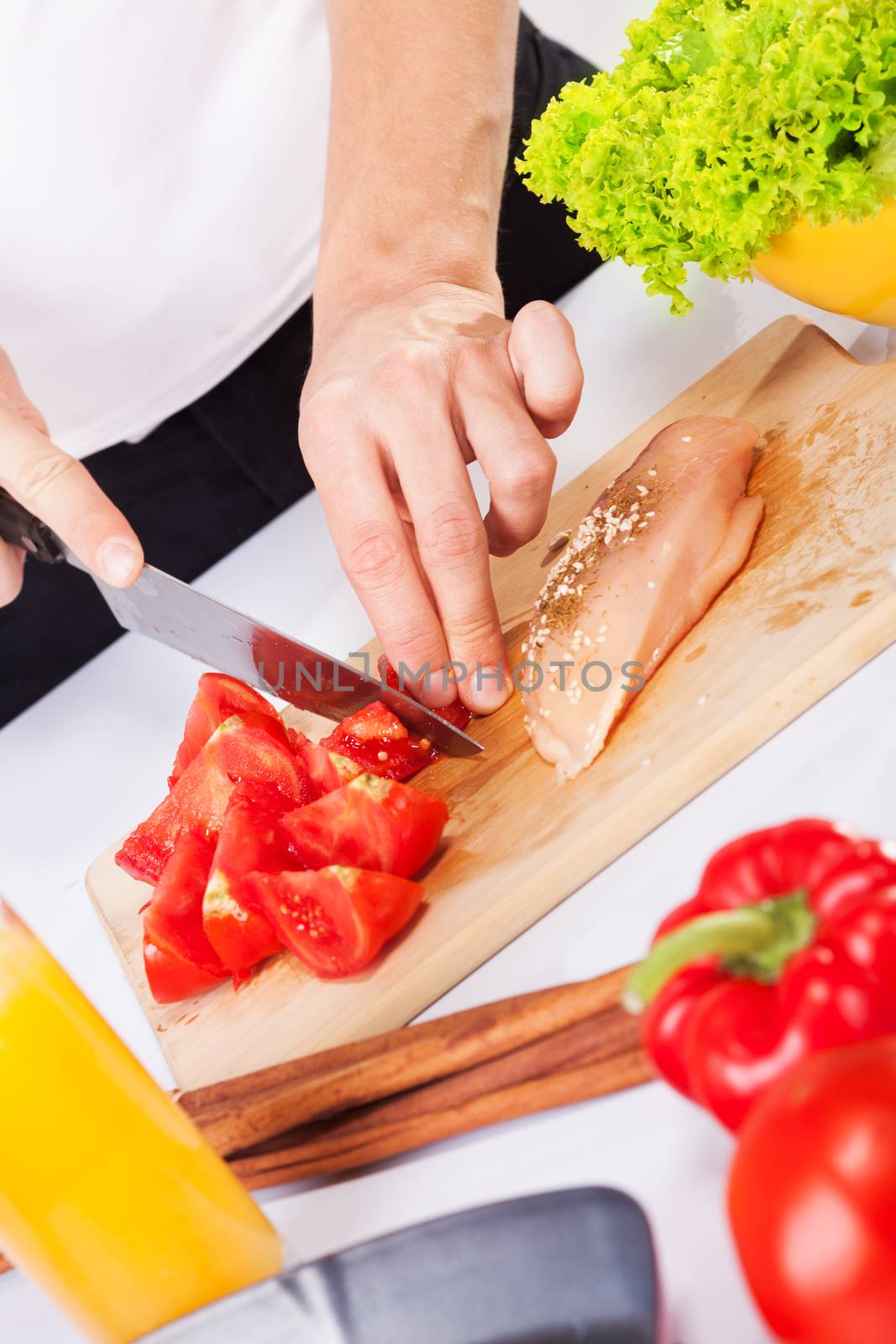 Cutting tomato and chicken breast in the cutting board.