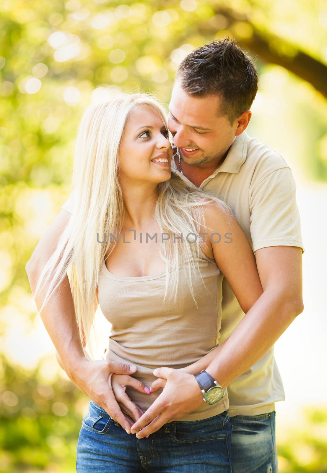Beautiful young romantic couple in the park and making heart shape with hands.