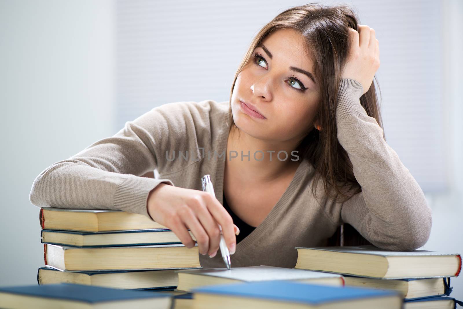 Tired student sitting with many books, with her head in hand.