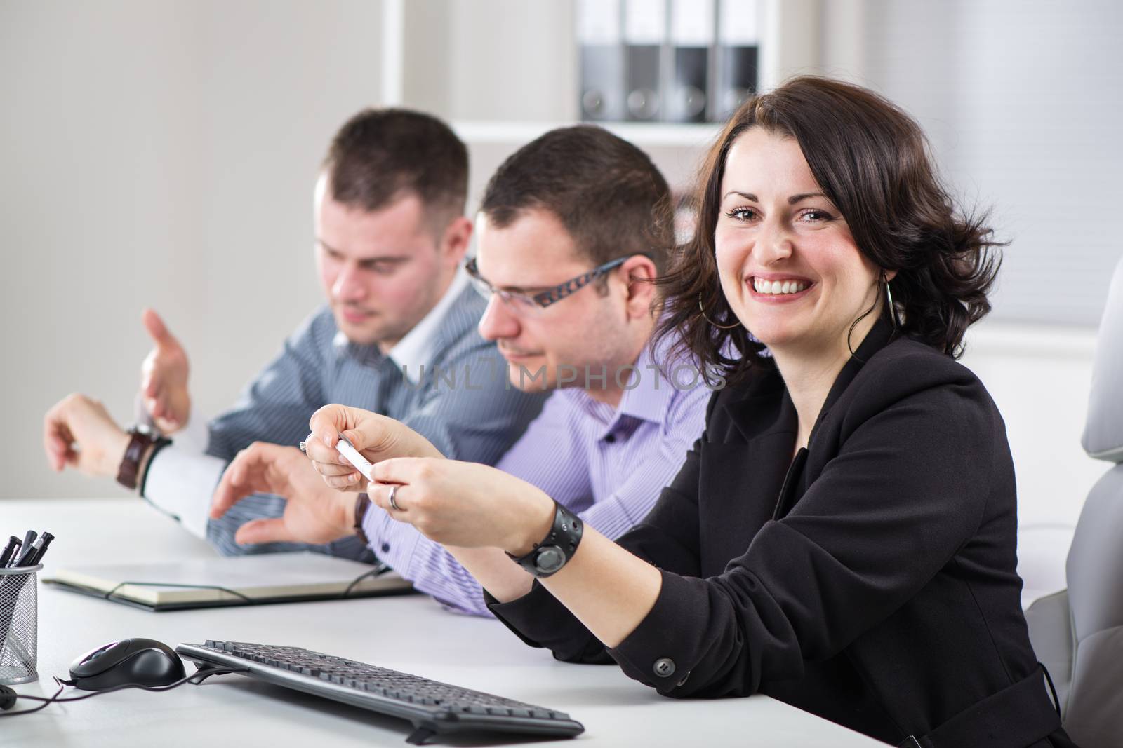 Happy Businesswoman sitting in the office. Looking at camera. His colleagues, in the background, watching the clock.