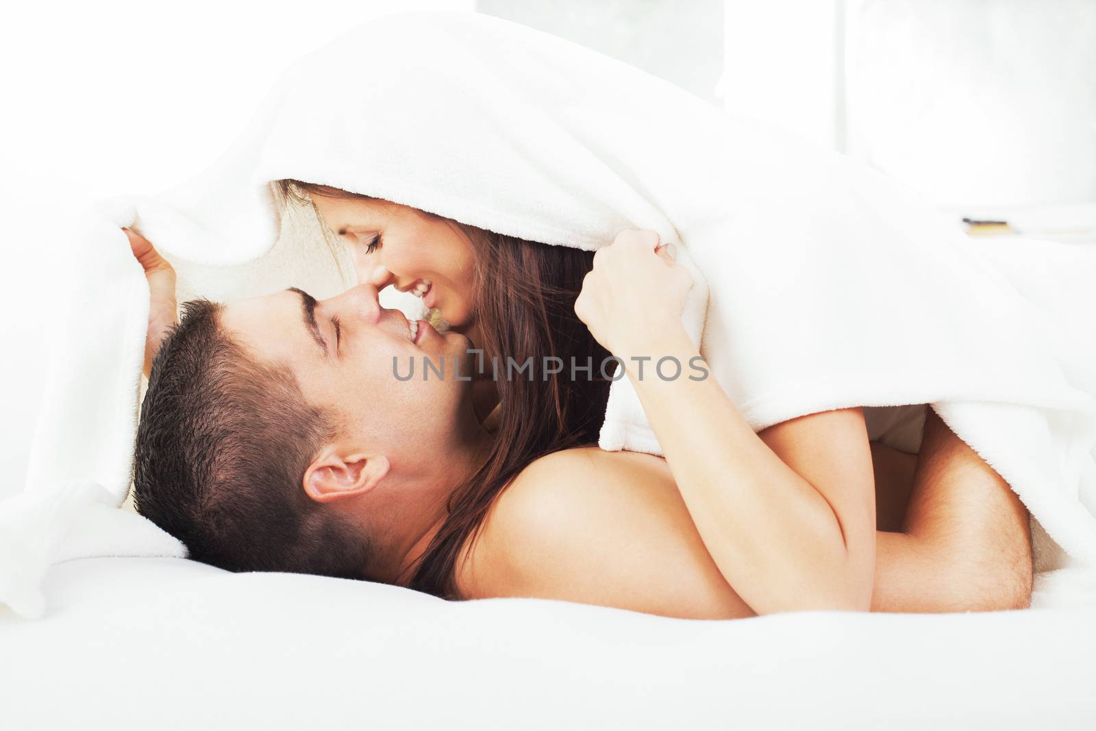 Beautiful romantic couple under blanket and touching noses.