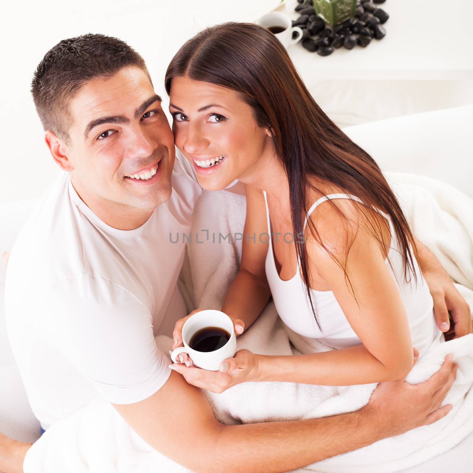 Young romantic couple in love sitting on the bed and drink coffee in the morning.