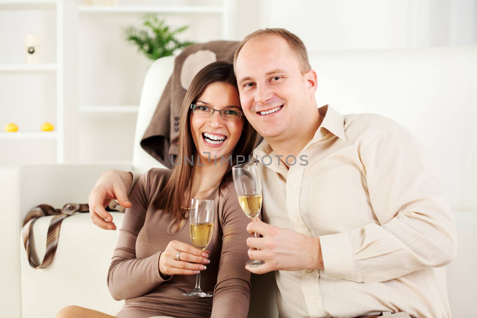 Happy Young couple sitting embraced at home, smiling and drinking  champagne.
