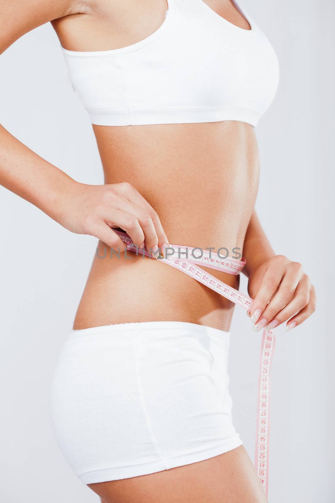 Beautiful young girl measuring perfect shape of waist.