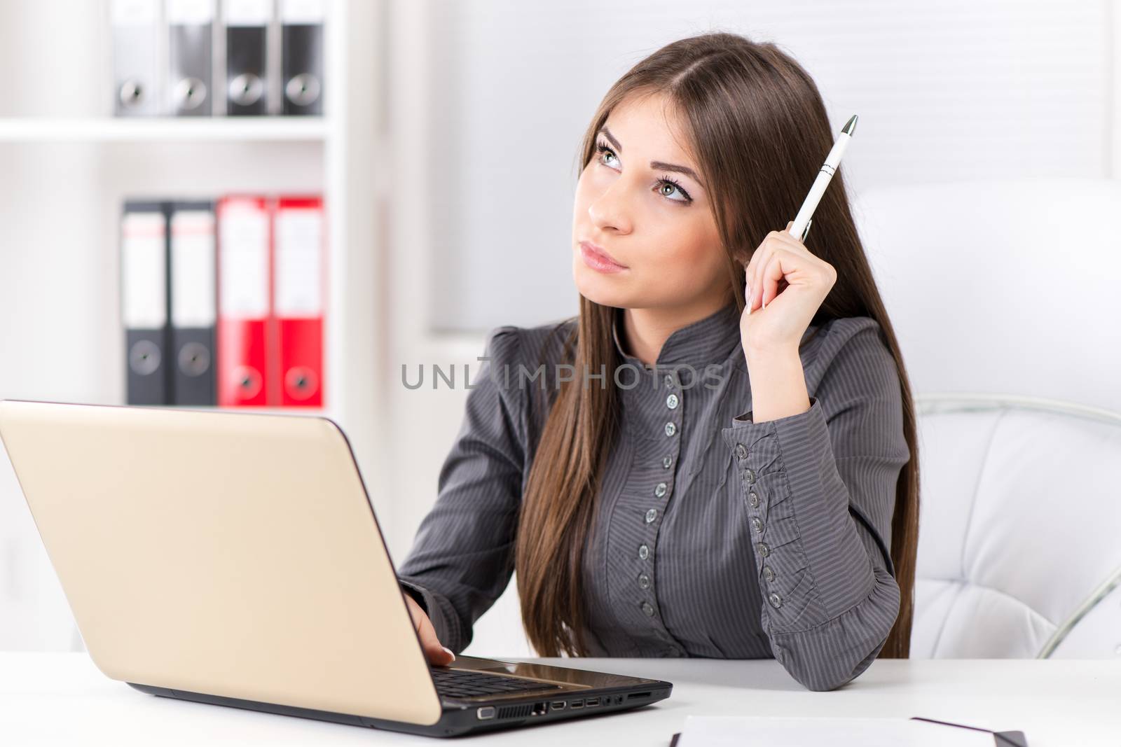 Businesswoman in the office, sitting, thinking and holding pencil in one hand. Having brilliant idea for business progress.