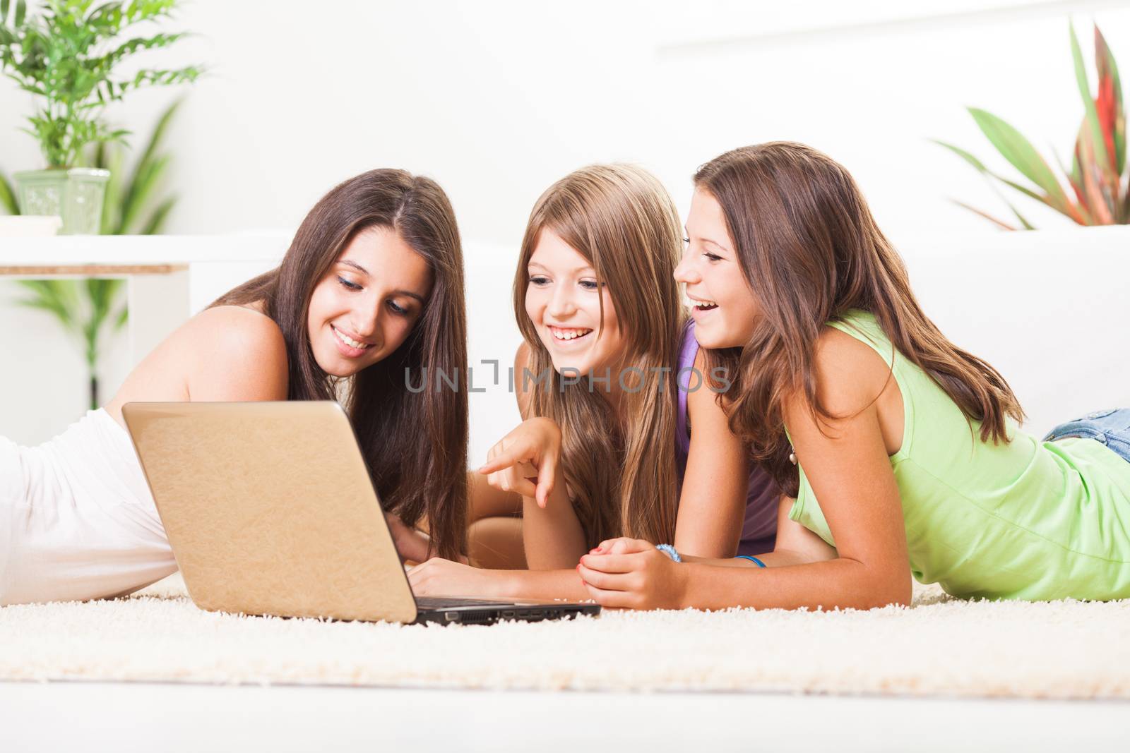 Beautiful teenage girls lying on the carpet with laptop and surfing in the internet.