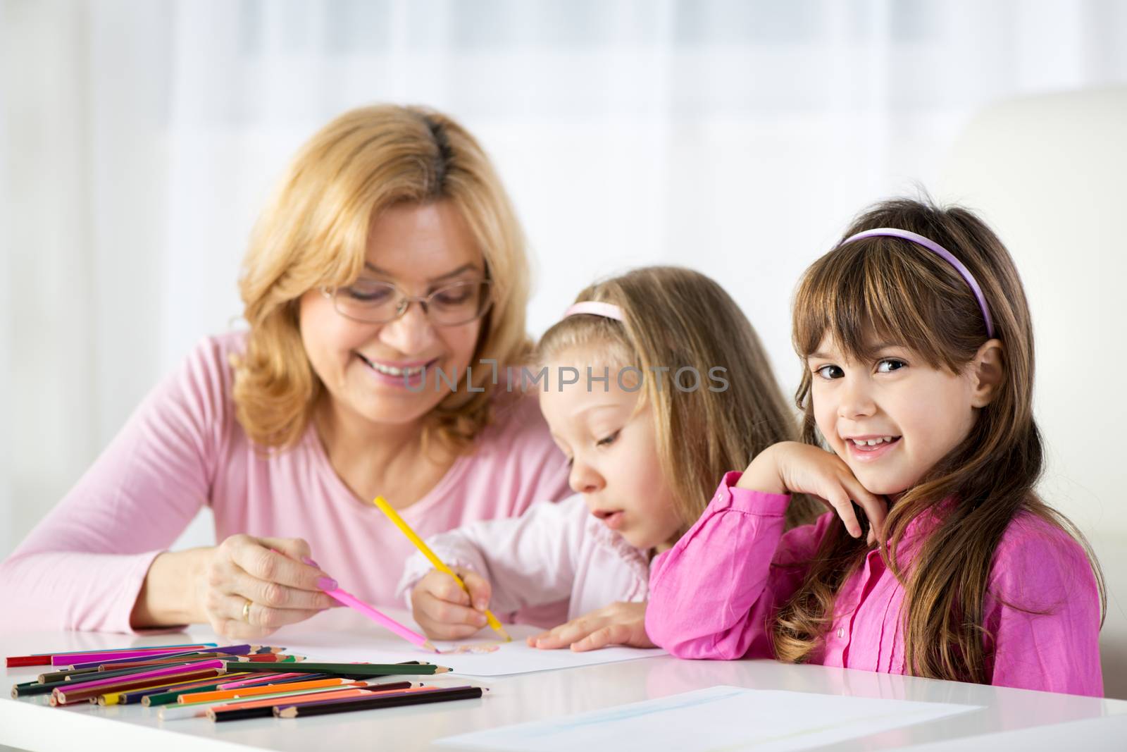 Two cute little girls drawing with colored pencils at home with Grandmother.