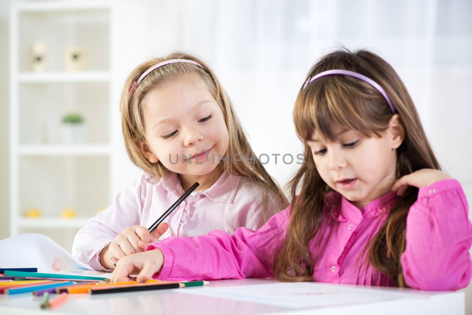 Two cute little girls drawing with colored pencils at home.