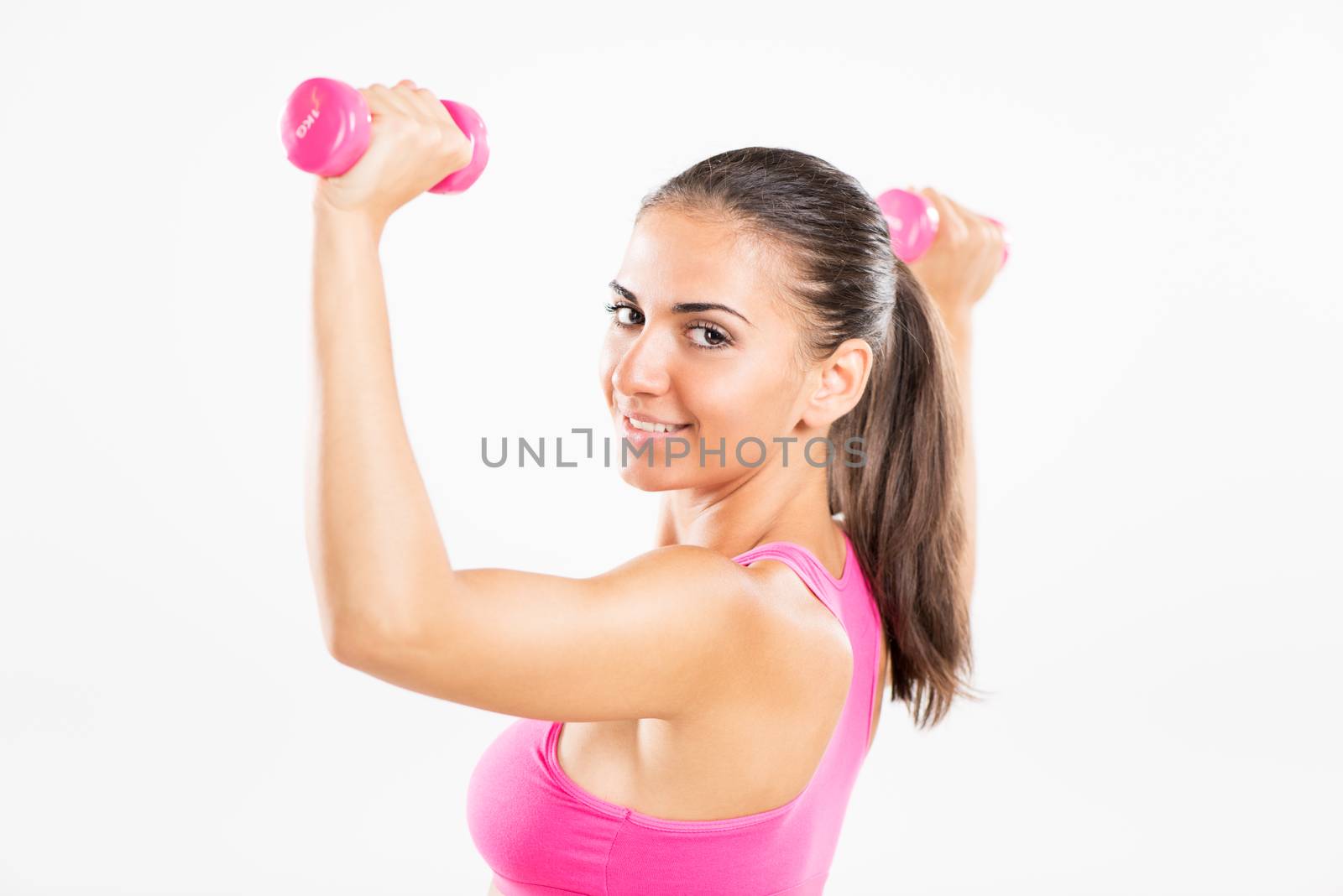 Portrait of a young beautiful woman exercising with dumbbells. She is practicing upper body muscle group.