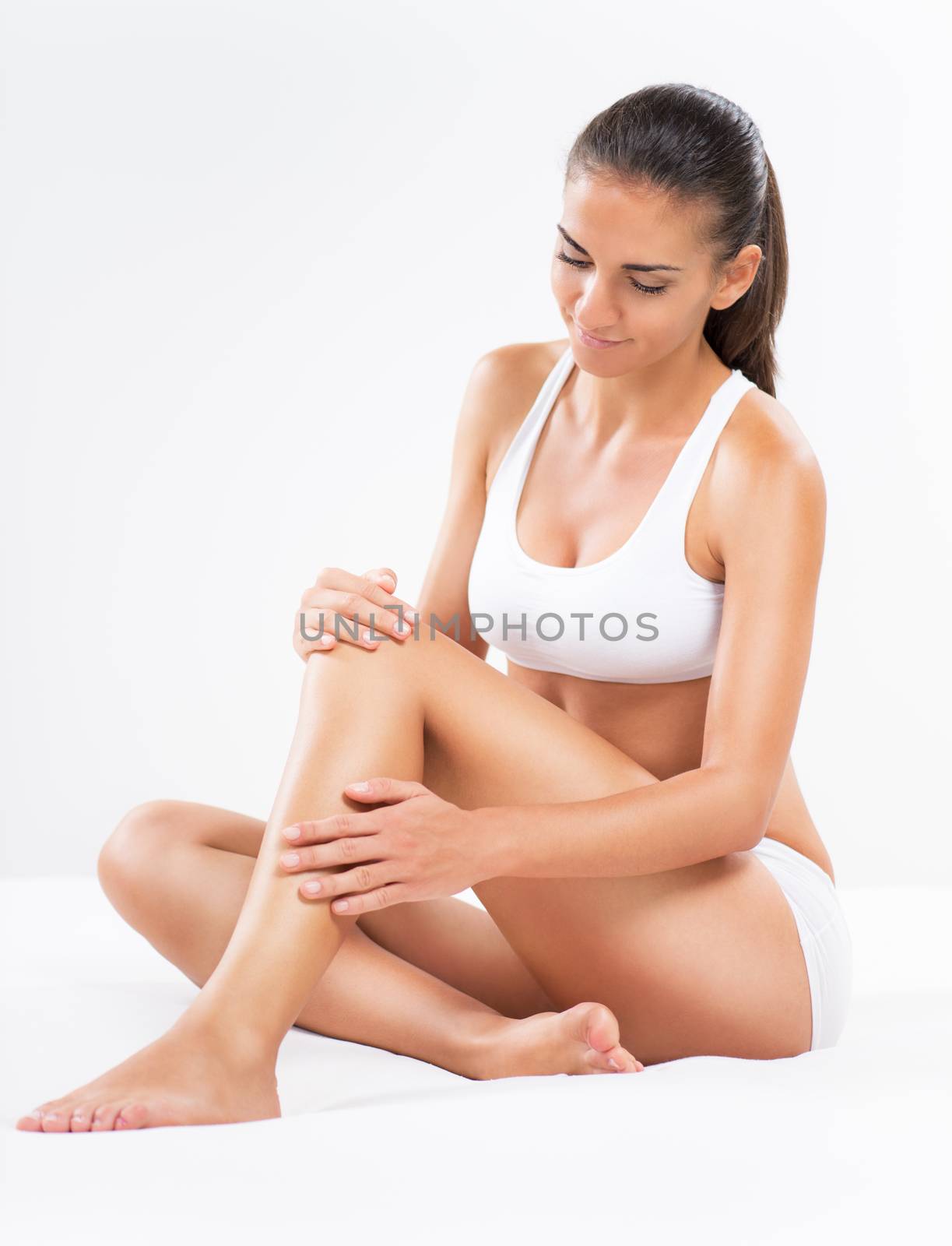 Beautiful young woman applying body lotion to her legs.