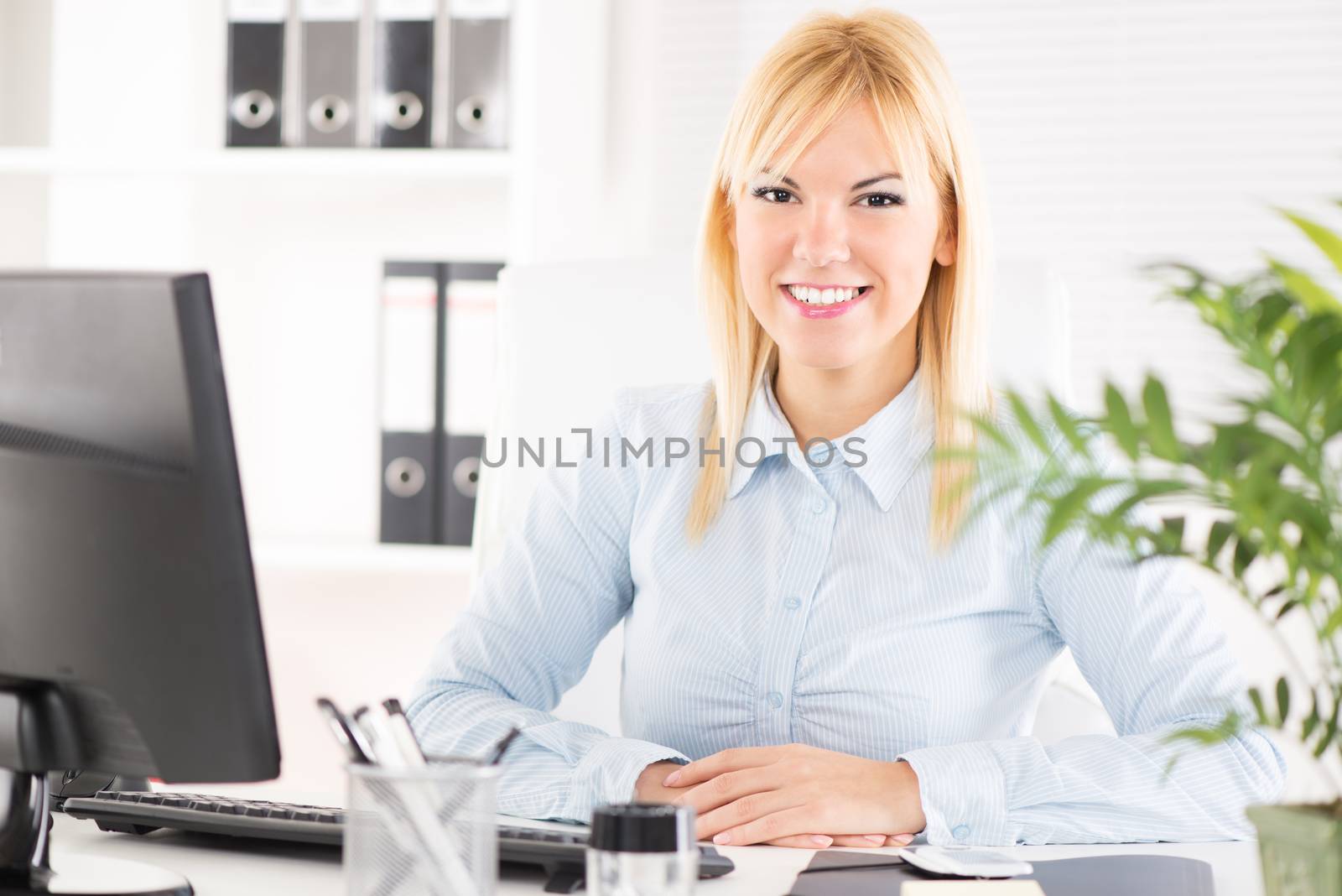 Businesswoman in the office. Sitting at the table with computer and Looking at camera.