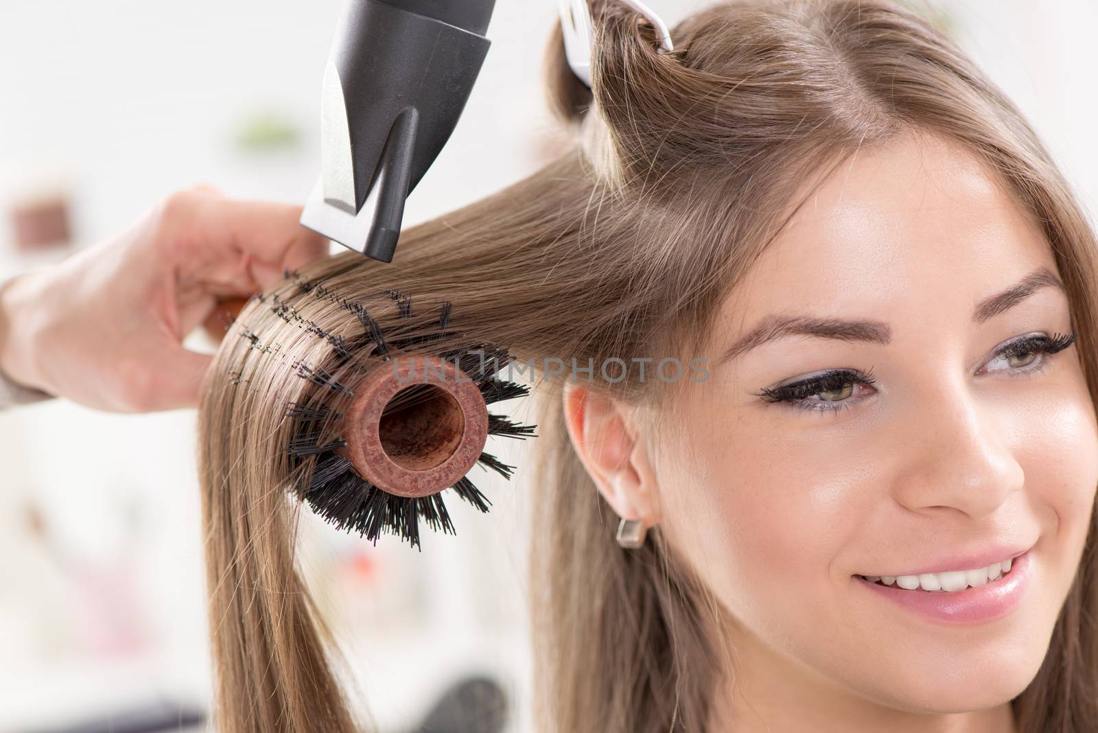 Hairdresser drying long brown hair with hair dryer and round brush. Close-Up.