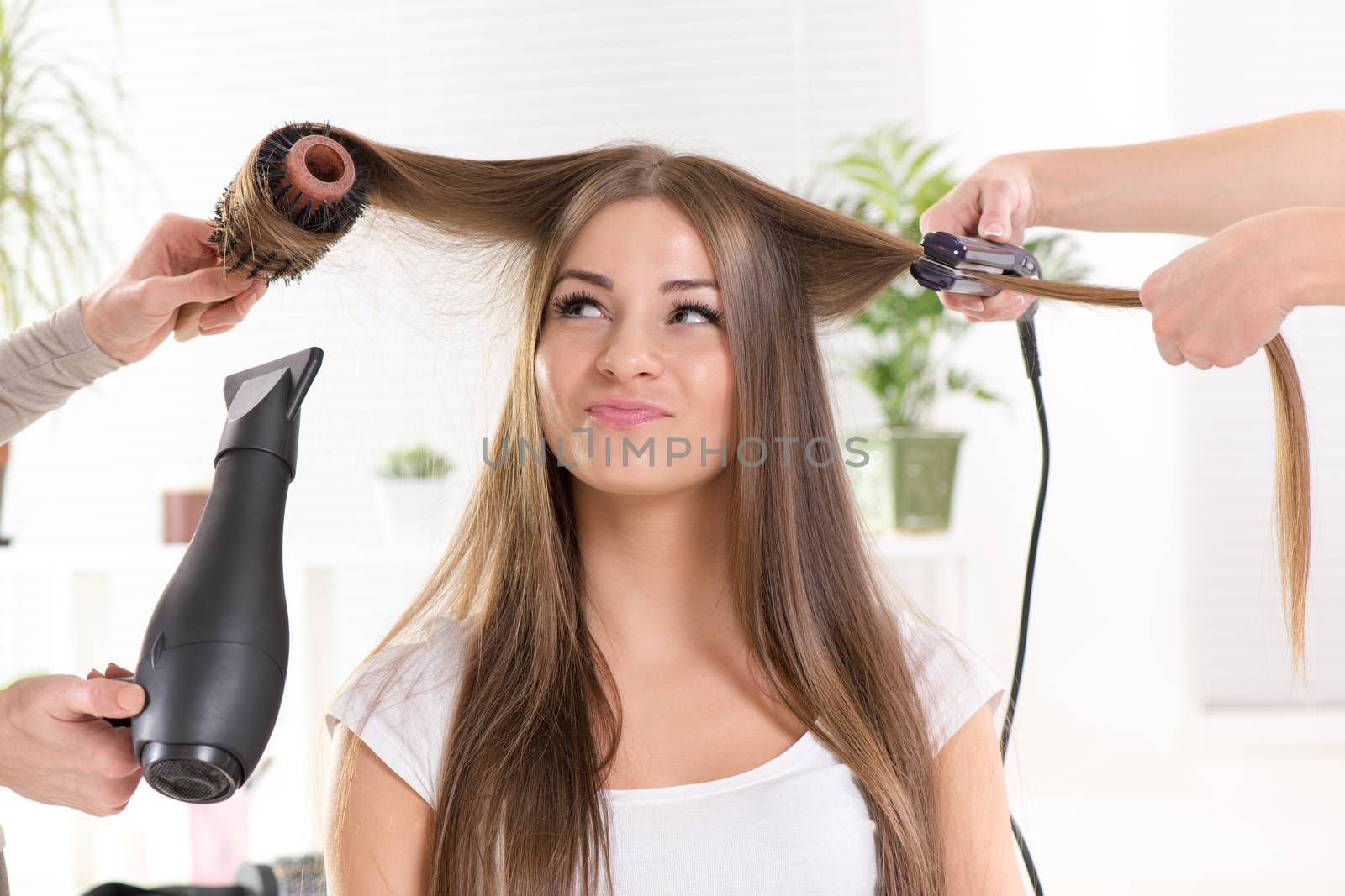 Hairdressers straightening long brown hair with hair dryer and round brush and hair irons.