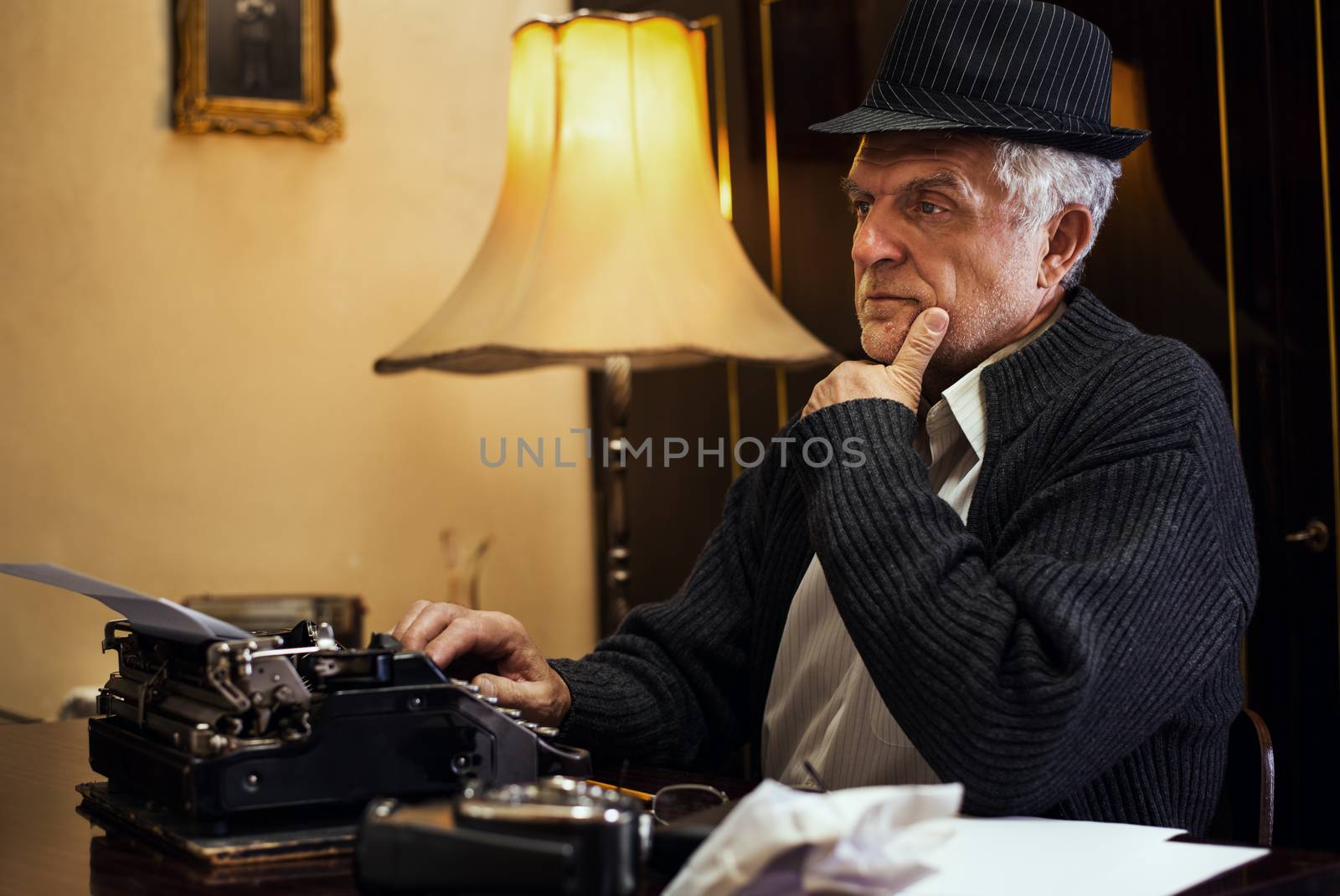Retro Senior Man writer with hat sitting at the Desk and thinking.