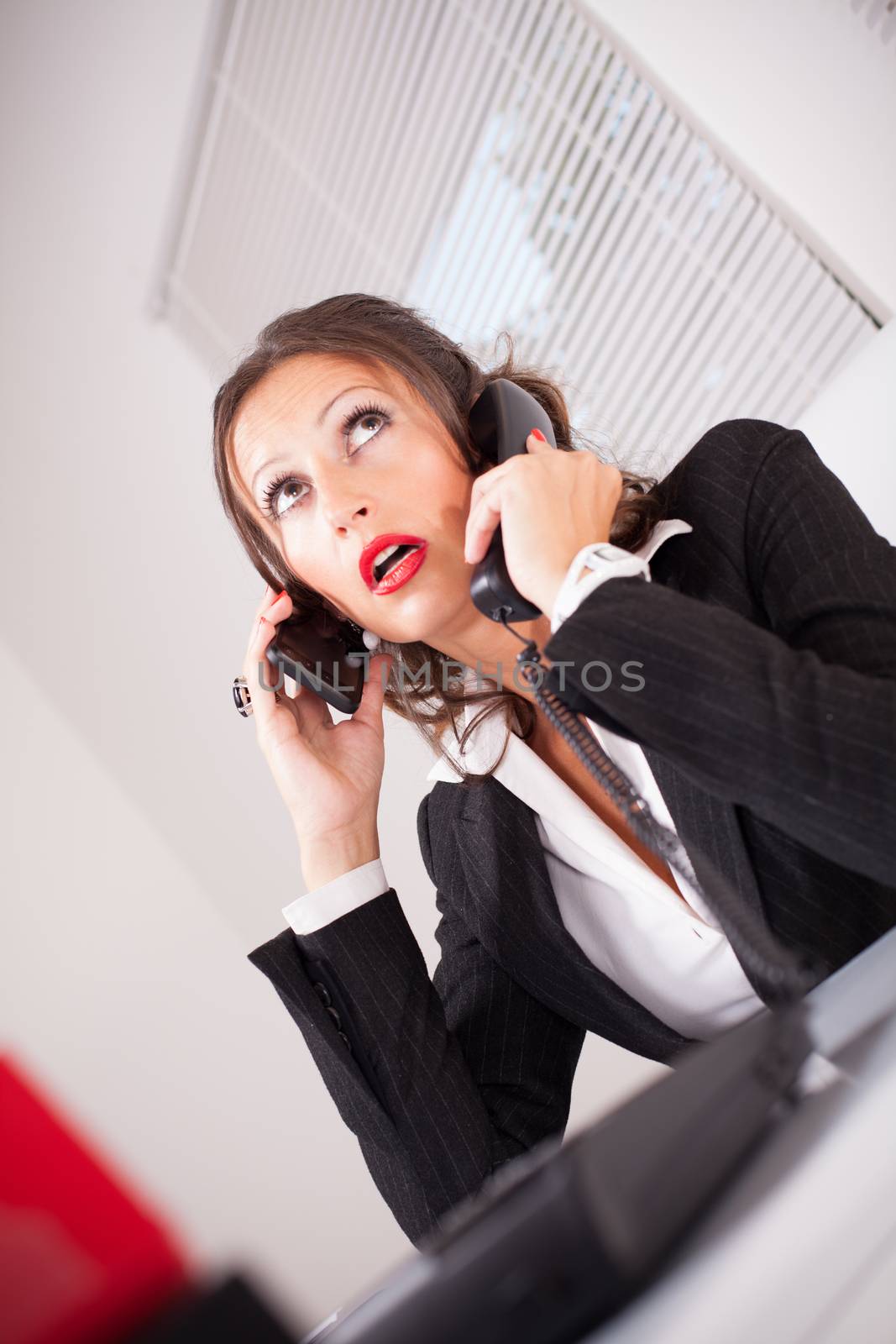 Attractive secretary is very busy. Talking in multiple phone in the same time, mobile and landline phone.