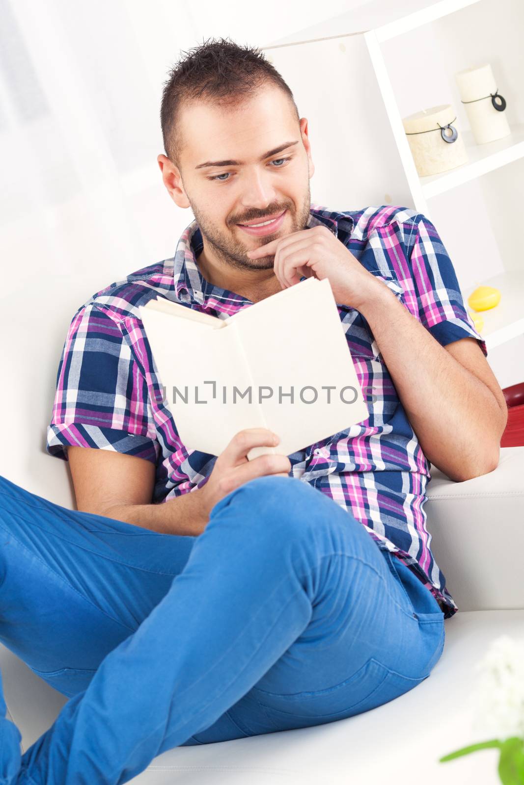 Beautiful young man resting with book at home.