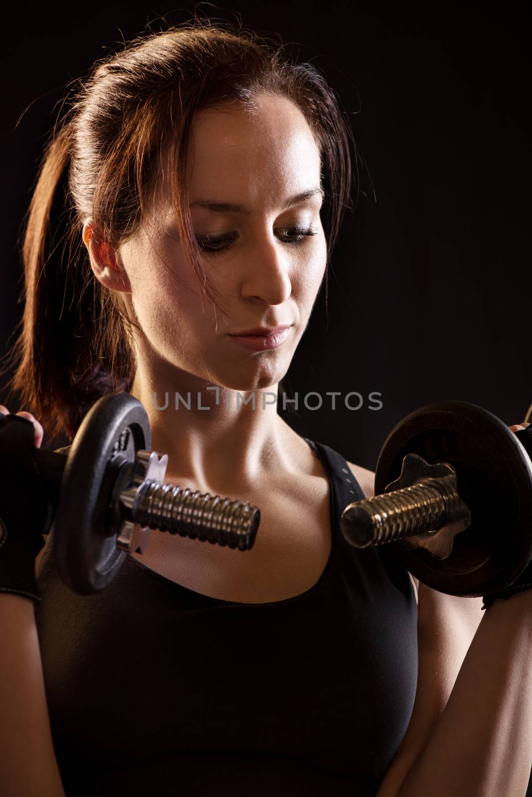 Portrait of a beautiful woman exercising with dumbbells on black background.