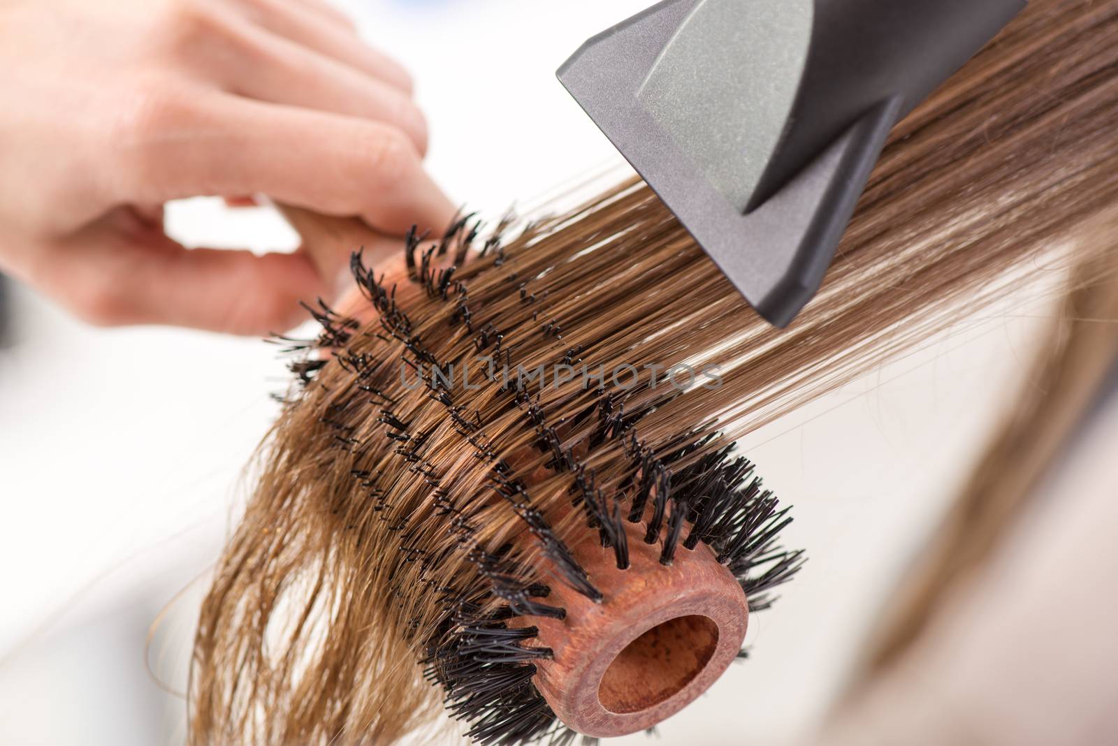 Drying long brown hair with hair dryer and round brush. Close-up.