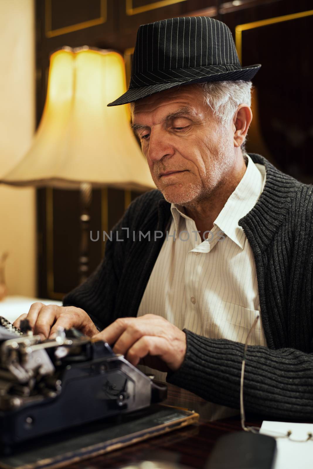 Retro Senior man writer with hat, writing on Obsolete Typewriter.